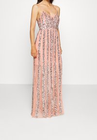 Lång rosa klänning med vertikala ränder av silverpaljetter, tunna spaghetti-axelremmar och en figurnära överdel med en flödande kjol.