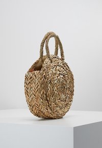 Borsa in paglia intrecciata a forma rotonda, con due manici testurizzati e apertura superiore, caratterizzata da un colore beige chiaro e un aspetto naturale e rustico.