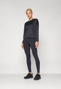 Black athletic long-sleeve top paired with black leggings and black sneakers. The top has a smooth texture and relaxed fit, while the leggings are form-fitting.