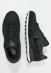 Svarta sportskor med överdel i mesh och mocka, texturerade accenter, vit mellansula och en blank svart Nike-logotyp på sidan.