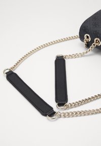 Černá kabelka s texturovaným povrchem, vybavená řetízkovým popruhem a koženými detaily. Výrazné zlaté kovové prvky zdůrazňují design.