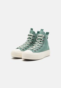 Zielone sneakersy typu high-top z płócienną cholewką, białymi sznurowadłami, okrągłym noskiem, gumową podeszwą i kontrastowymi detalami w stębnowaniu. Posiadają solidne oczka i pętle do zakładania.