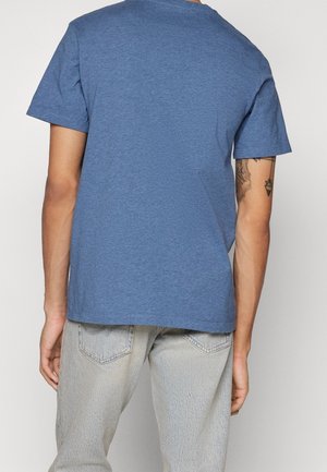 Blaues T-Shirt mit kurzen Ärmeln aus softem Stoff und Rundhalsausschnitt. Trägt eine hellfarbige Jeans und zeigt ein minimalistisches Design.