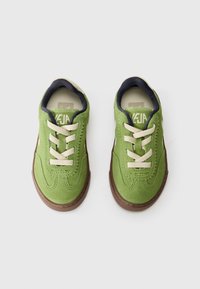 Πράσινα σουέτ αθλητικά παπούτσια με μπεζ κορδόνια, ναυτικές εσωτερικές επενδύσεις και καφέ καουτσούκ σόλες. Διαθέτουν ραφή κατά μήκος των πλαϊνών και λογότυπο στην γλώσσα.