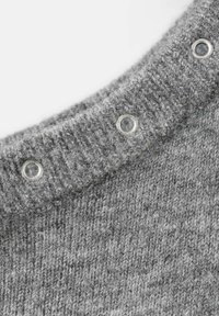 Sivi pleteni džemper s rebrastim ovratnikom i srebrnim ringlama. Tekstura je mekana i labavo tkanja, naglašavajući ležerni dizajn.