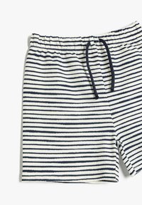Hvide shorts med vandrette marineblå striber og en marineblå snor i en elastisk talje mod en hvid baggrund.