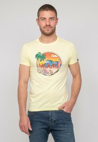 T-shirt en coton jaune avec un imprimé graphique représentant "MIAMI Sunset", des palmiers et des vagues. Manches courtes, col rond, design ajusté.
