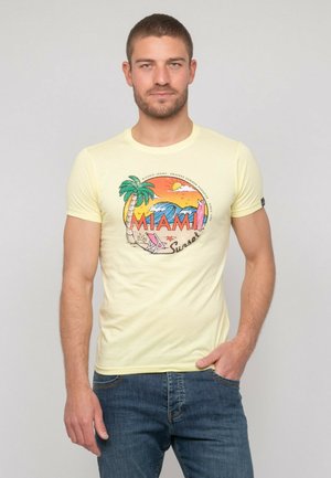 T-shirt en coton jaune avec un imprimé graphique représentant "MIAMI Sunset", des palmiers et des vagues. Manches courtes, col rond, design ajusté.