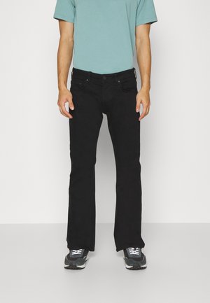 Svarta raka jeans med en slät textur. Pairade med en ljusblå T-shirt och grå träningsskor med svarta detaljer.