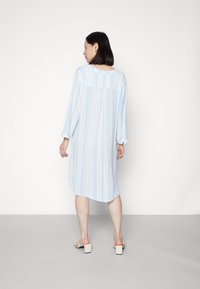 Vestido listrado azul claro com mangas longas e decote arredondado, feito de um tecido suave, apresentando pregas verticais e um corte relaxado.