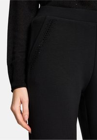 Czarne spodnie dresowe wykonane z miękkiej tkaniny posiadają boczną kieszeń ozdobioną rzędem czarnych elementów, które dodają tekstury i detali konstrukcji.