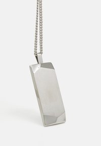 Pendentif en argent de forme rectangulaire, avec une texture brossée, des bords angulaires et une chaîne. Marque gravée visible.