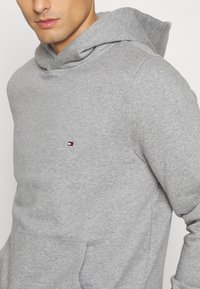 Felpa grigia realizzata in morbido tessuto misto cotone. Presenta una tasca a marsupio e un piccolo logo ricamato in rosso, bianco e blu sul petto.