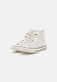 Høje sneakers i hvid læder med blomstrede applikationer, sort gummisål og kontrasterende sort stribe langs sålen.
