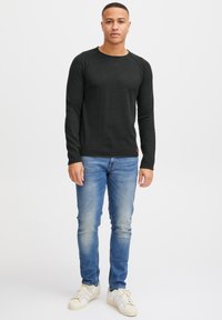Svart langermet strikket skjorte med rund hals, kombinert med lyseblå slim-fit jeans og hvite sneakers. Enkel, uformell design.