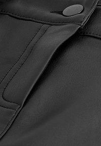 Tissu en cuir noir avec une texture lisse, présentant des coutures piquées et un accent en bouton noir circulaire. Gros plan sur les détails du matériau.