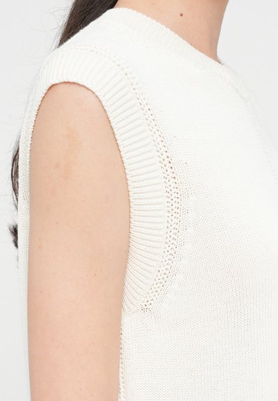 Top senza maniche lavorato a maglia color avorio con scollatura rotonda a costine e cuciture sulle spalle. Presenta dettagli a lavoro aperto vicino alle ascelle.