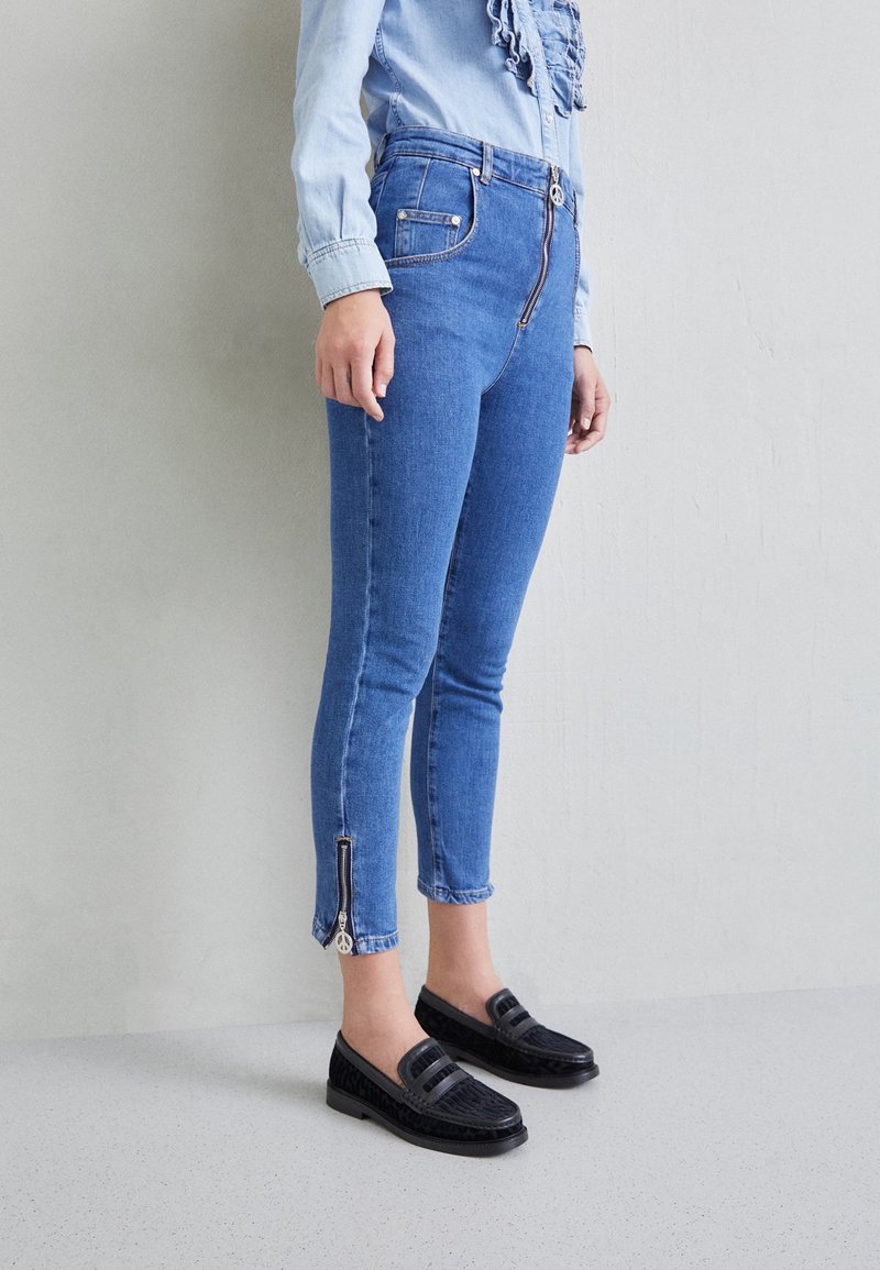Modré džíny skinny střihu z denimu s detailním zipem na kotnících, s polovičním pasem a předními kapsami, doplněné černými mokasínami.