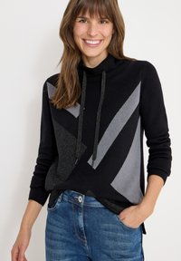 Maglione a fantasia nera e grigia con collo a cowl e cordoncini, caratterizzato da disegni geometrici e una vestibilità comoda, abbinato a jeans blu.