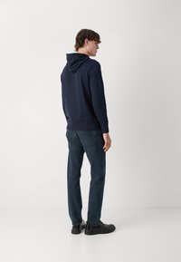 Sudadera navy con capucha ajustable, textura suave y puños acanalados, combinada con jeans de mezclilla oscura y calzado negro.