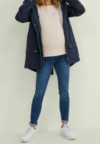 Námořnická nepromokavá parka s kapucí, pod ní světle pruhovaný top, doplněná modrými úzkými džíny a bílými teniskami.