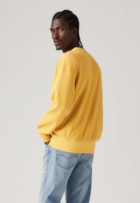 Yellow sweatshirt with long sleeves, ribbed cuffs, and a round neckline. Paired with light blue loose-fitting jeans. Smooth texture.
