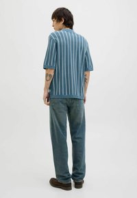 Haut en tricot à rayures bleu et blanc à manches courtes avec une coupe décontractée, associé à un jean léger bleu clair à coupe ample et des chaussures marron.