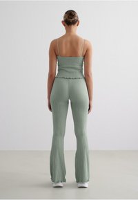 Two-piece outfit in soft green ribbed fabric, featuring a fitted, cropped top with spaghetti straps and flared pants with ruffled hems.
