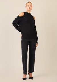 Czarny sweter dziany z wycięciami na ramionach, w połączeniu z czarnymi dżinsami z srebrnymi zdobieniami. Buty to czarne szpilki.