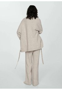 Bežový pletený sveter a zodpovedajúce nohavice s voľným strihom, bočnými šnúrkami a jemnou textúrou, zobrazené zozadu na svetlom pozadí.