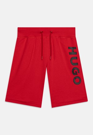 Shorts rouges arrivant au genou avec une taille élastique et des cordons de serrage, présentant un grand texte noir "HUGO" verticalement sur la jambe droite.