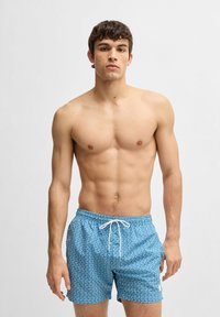 Blå badbyxor med geometrisk mönster, dragsko i midjan och en liten logoprydnad. Tyget verkar lätt och snabb-torkar.