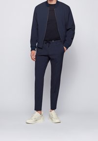 Marinblå bomberjacka med ribbad mudd, svart t-shirt, skräddarsydda marinblå byxor och ljusa sneakers. Minimalistisk design och strömlinjeformad passform.