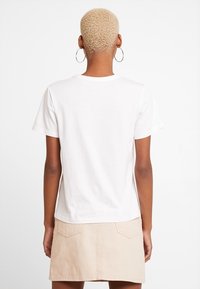 Krótki rękaw, biały bawełniany t-shirt o luźnym kroju, z okrągłym dekoltem i gładką fakturą, zestawiony z beżową spódnicą dżinsową.