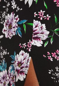 Sort stof med store, levende blomster mønstre i hvid, lilla og pink med grønne blade; sideslidsdetalje synlig.