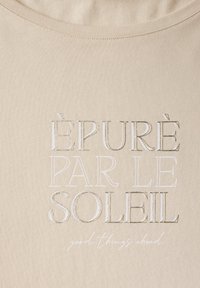 Béžové bavlněné tričko s výšivkou textu: "ÉPURÉ PAR LE SOLEIL" a "dobré věci vpřed" v kurzívě. Lehká, měkká textura.