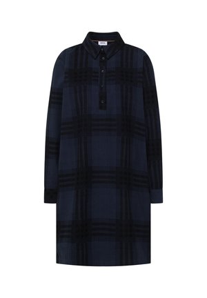 Femme aux cheveux bruns portant une robe chemise à manches longues avec un motif à carreaux bleu marine et noir vue de dos sur un fond uni.