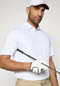 Λευκό πόλο πουκάμισο με σχέδια σε ανοιχτό μπλε ασπίδα και σταυρό, κοντά μανίκια και γιακά. Διακοσμημένο με μπαστούνι του γκολφ και λευκό γάντι.