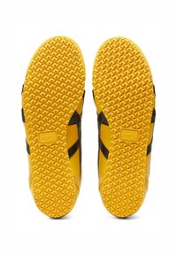 Černé a žluté sportovní boty s texturovanou gumovou podrážkou s diamantovým vzorem a logem. Na stranách mají kontrastní černé akcenty.