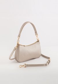 Bolso de mano beige con una textura suave, forma curva y cierre de cremallera. Cuenta con herrajes dorados y una correa ajustable.