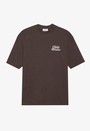 T-shirt in cotone marrone scuro, maniche corte, collo rotondo, presenta la scritta "Rivelazione Cosmica" in bianco sul lato sinistro del petto. Tessuto morbido, vestibilità rilassata.