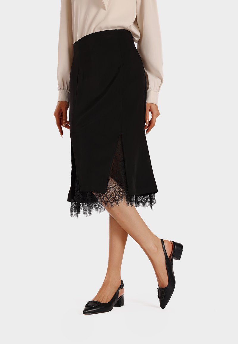 Gonna nera a matita con orlo in pizzo, caratterizzata da spacchi laterali, abbinata a scarpe nere con tacco e una blusa chiara. Tessuto liscio.