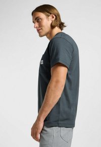 Maglietta a maniche corte grigio scuro con taschino sul petto, realizzata in cotone con una texture liscia. Design minimalista con un piccolo etichetta.