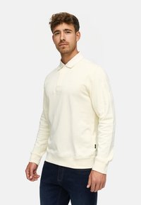 Kremfarget langermet polo-skjorte med krage, som har en knappestolpe og ribbede mansjetter. Myk stoff med minimal merkevare.