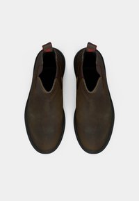 Rjavi usnjeni copati brez vezalk z elastičnimi stranskimi paneli in nizkim profilom. Imajo črni gumijasti podplat in kontrastni rdeči jeziček za poteg.