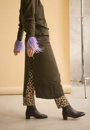 Vestido verde oliva con una abertura lateral superpuesto sobre pantalones de leopardo, con puños de plumas lavanda y botas de tobillo marrones.