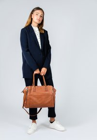 Brun læderhåndtaske med dobbelt hanke, lynlåslomme, glat tekstur og minimalistisk design. Remme sikret med rektangulære detaljer.