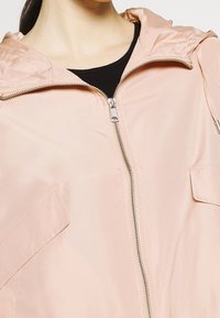 Jasnoróżowa kurtka z zapinanym przodem, kapturem i bocznymi kieszeniami. Wykonana z gładkiego materiału o lekkiej konstrukcji.