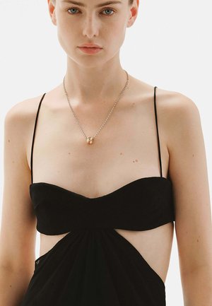 Vestido negro con cortes a los lados y tirantes finos. Tela suave con un corsé ajustado y una falda fluida. Collar de plata con un colgante de oro.