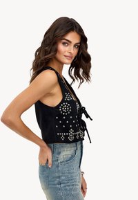 Zwarte suède crop top met versieringen, voorzien van een v-hals, zijcut-outs en een frontale strik. Gepaard met een vervaagde blauwe denim rok.